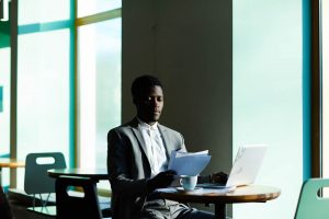 Homem negro vestido de terno segurando papéis em frente a um notebook representando a importância do uso e da interpretação de dados em escritórios de advocacia
