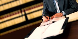 Imagem de corpo masculino de terno escrevendo em livro representando monitoramento de processos jurídicos