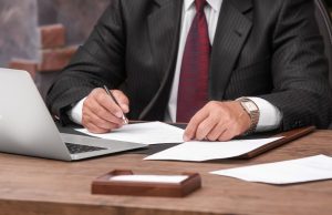 Imagem corpo de homem de terno em frente a um notebook e papéis representando como otimizar o gerenciamento de pautas de audiências e prazos