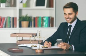Imagem de homem de terno sentado, sorrindo, segurando celular em uma mão e caneta na outra, ilustrando inteligência jurídica termo em alta na advocacia