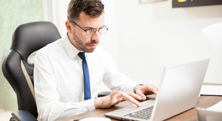 Homem branco de barba e óculos sentado em frente a notebook pesquisando sobre os erros mais comuns em peças jurídicas